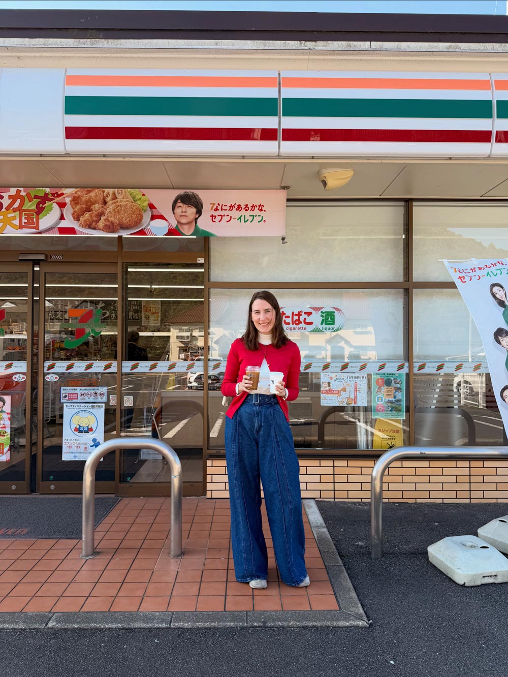 nele holding two coffees standing in front of a 7-eleven convenience store in japan
