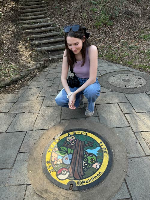 nele sitting near the caterpie, weedle and oddish manhole cover in serigaya park, machida tokyo on a sunny day
