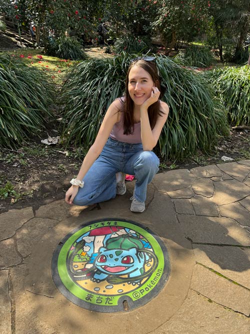 nele smiling next to bulbasaur manhole cover in machida tokyo on a sunny day