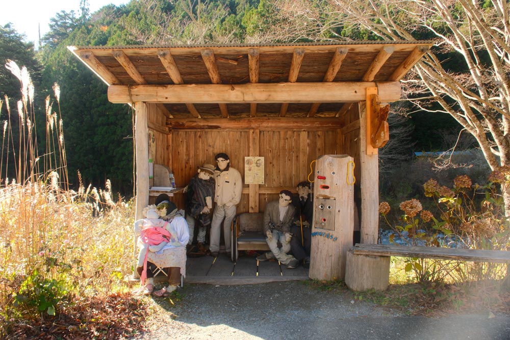 scarecrows in nagoro sitting at a bus stop on a sunny day