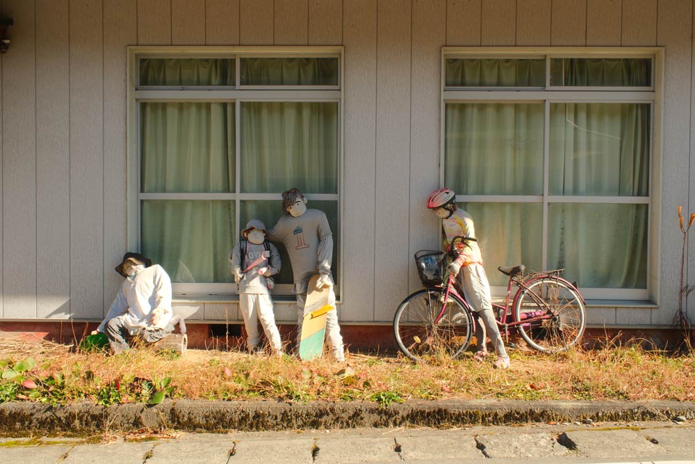 scarecrows in nagoro near an abandoned building with a bike