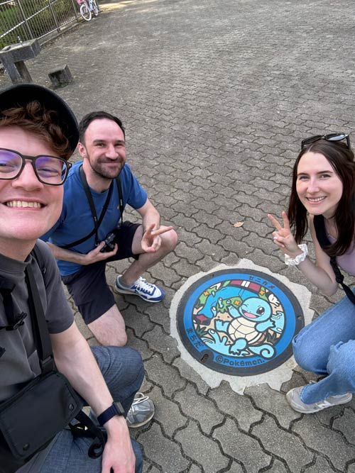 nele richard and friend sitting near the squirtle manhole cover in machida tokyo on a sunny day